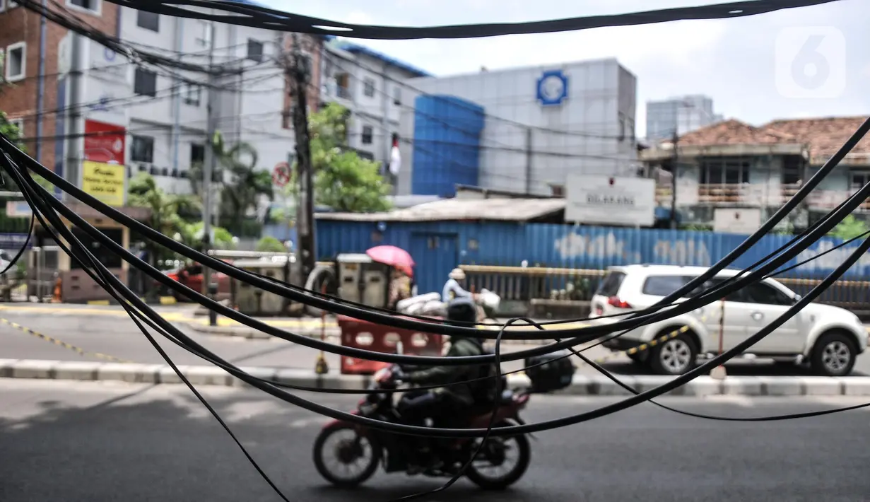 Kendaraan melintas di dekat jaringan kabel utilitas yang menjuntai di Jalan Proklamasi, Pegangsaan, Kecamatan Menteng, Jakarta Pusat, Kamis (6/10/2022). Minimnya pengawasan dalam tahap penyelesaian proyek revitalisasi trotoar oleh pihak terkait menyebabkan jaringan kabel utilitas di kawasan tersebut semrawut  yang dapat membahayakan keselamatan pengguna jalan, terutama saat musim penghujan. (merdeka.com/Iqbal S. Nugroho)