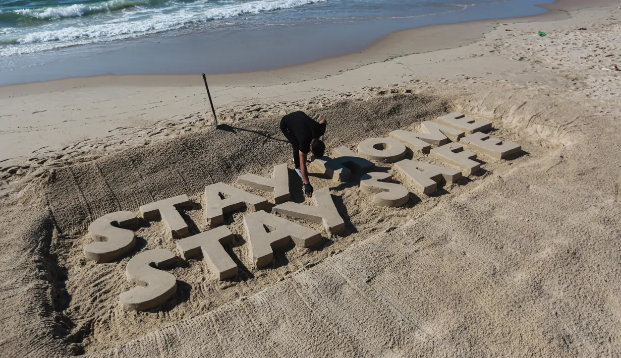 Seorang seniman Palestina mengukir kata "TETAP DI RUMAH TETAP AMAN" dengan pasir di sebuah pantai di Gaza City pada 12 April 2020. Palestina pada Minggu (12/4) melaporkan jumlah total kasus COVID-19 di negara tersebut telah mencapai 290. (Xinhua/Rizek Abdeljawad)