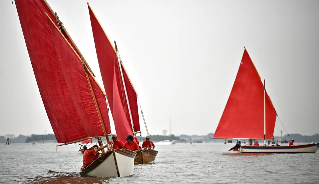 Anggota asosiasi pelayaran budaya berlayar dalam acara Regatta Merah di Venesia, Italia, Minggu (20/6/2021). Regatta Merah diselenggarakan oleh seniman AS Melissa Mc Gill. (MARCO BERTORELLO/AFP)