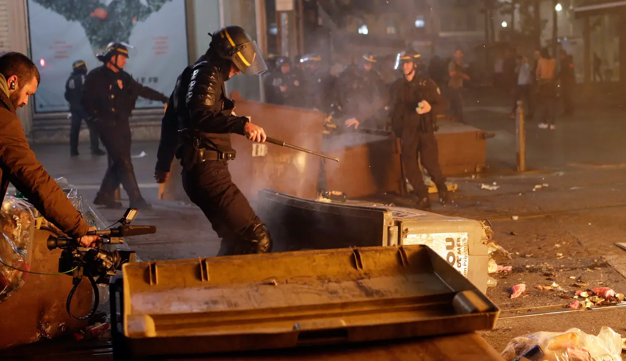 Polisi anti huru hara berjalan melewati tempat sampah yang dibakar oleh para pendukung Marseille di Marseille, Prancis (16/5). Kerusuhan ini disebabkan oleh fans Marseille yang tidak terima timnya kalah dalam final Liga Europa. (AP / Claude Paris)