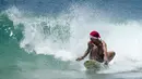 Seorang pria bertopi Santa memegang kamera aksi di giginya saat berselancar saat merayakan Natal di Pantai Bondi di Sydney, Sabtu (25/12/2021). (AP Photo/Rick Rycroft)