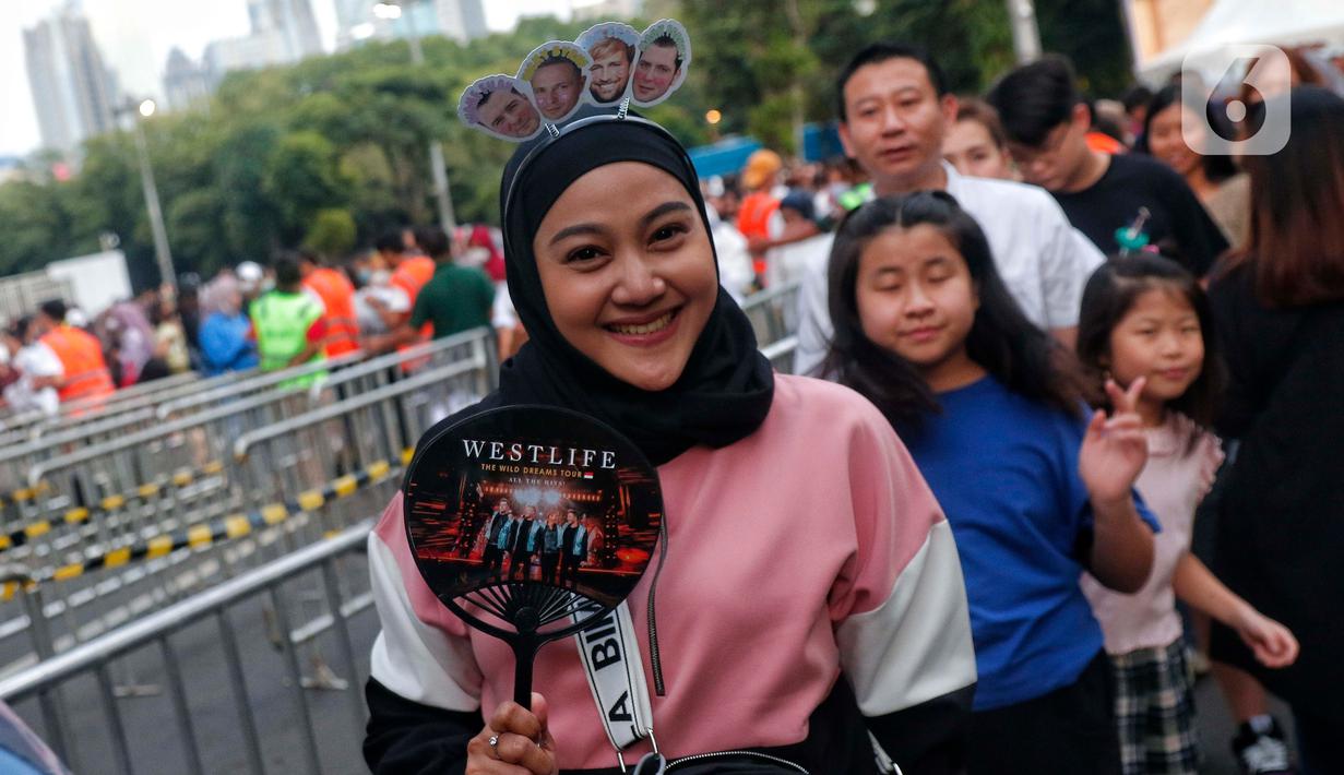 Seorang penggemar Westlife berpose saat tiba untuk menonton konser bertajuk 'The Wild Dreams Tour 2023' di kawasan Stadion Utama Gelora Bung Karno Sabtu (11/2/2023). Penampilan Westlife menjadi penantian penggemar yang datang dari berbagai daerah. Bahkan, sebagian penggemar juga datang dari sejumlah kota di luar Jabodetabek. (Liputan6.com/Angga Yuniar)