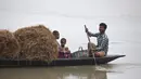 Keluarga membawa jerami untuk ternak mereka di atas kapal ketika mereka menyeberangi sungai Brahmaputra di desa Kasoshila di pinggiran Gauhati, India (21/10/2019).  (AP Photo/Anupam Nath)