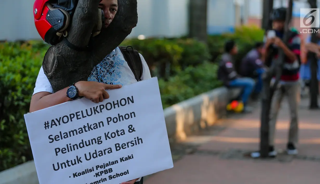 Seorang pria memeluk pohon sambil membentangkan poster saat menggelar aksi #ayopelukpohonini di Jalan Sudirman, Jakarta, Jumat (22/9). Pohon-pohon tersebut akan dipindahkan karena adanya proyek pelebaran trotoar. (Liputan6.com/Faizal Fanani)