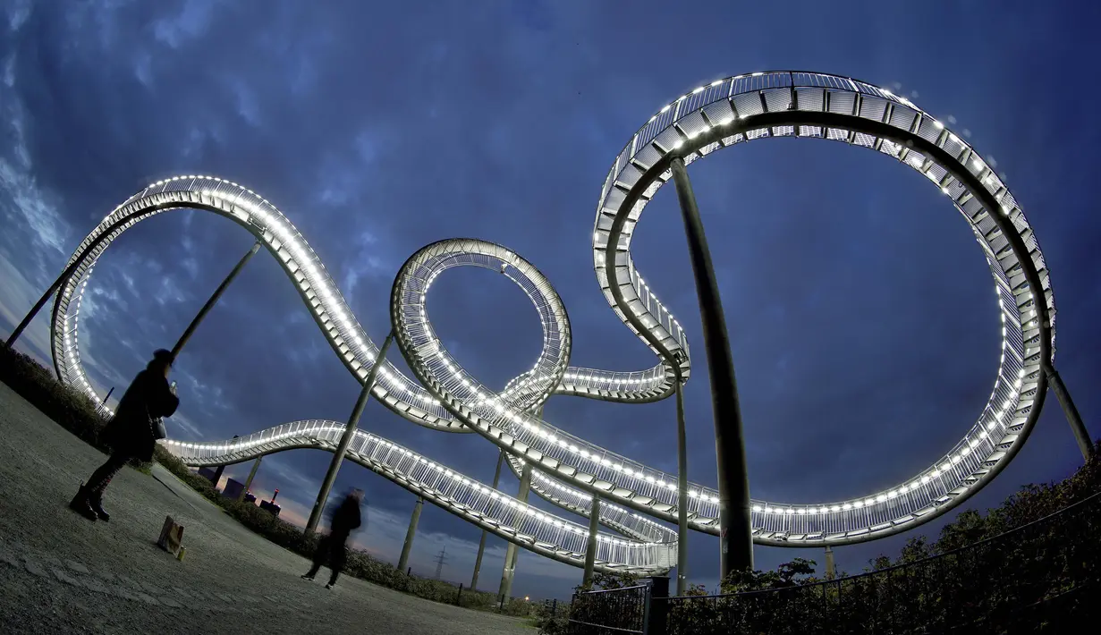 Pengunjung mengambil gambar patung jalur roller coaster 'Tiger and Turtle - Magic Mountain' yang ditutup akibat pembatasan virus corona di Duisburg, Jerman, 19 Oktober 2020. (AP Photo/Michael Sohn)