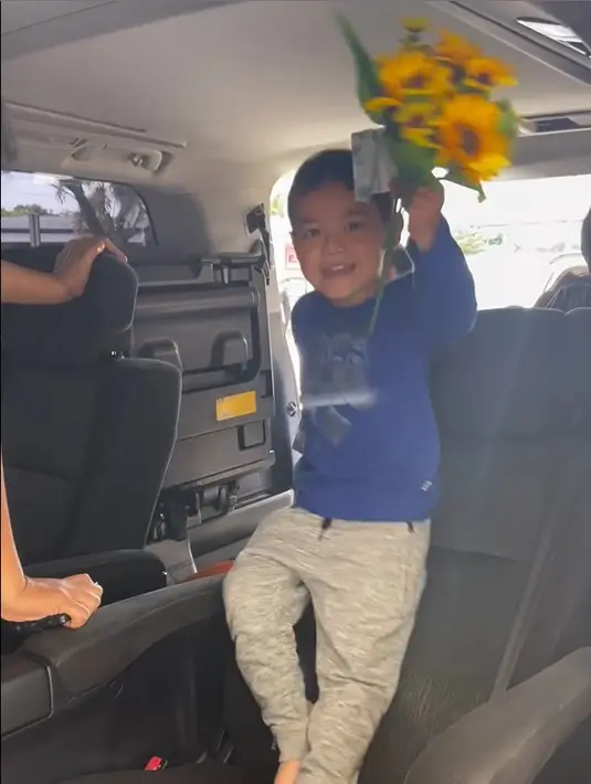 Abimanyu Manggala Nugroho Putro senyum saat ibundanya akan naik mobil. Sedangkan di tangannya memegang bunga dan uang kertas pecahan dua ribu. [Instagram/vickyshu]