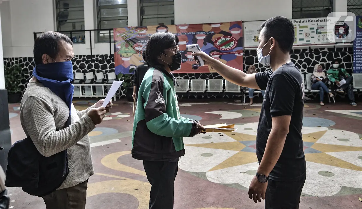 Petugas memeriksa suhu tubuh warga yang hendak mengambil BST di SMPN 3, Jakarta, Selasa (26/1/2021). Pencairan BST di Jakarta yang dilakukan Bank DKI bersama Dinsos DKI Jakarta dibatasi hanya 500 orang penerima per titik per hari demi menghindari penyebaran COVID-19. (merdeka.com/Iqbal S. Nugroho)