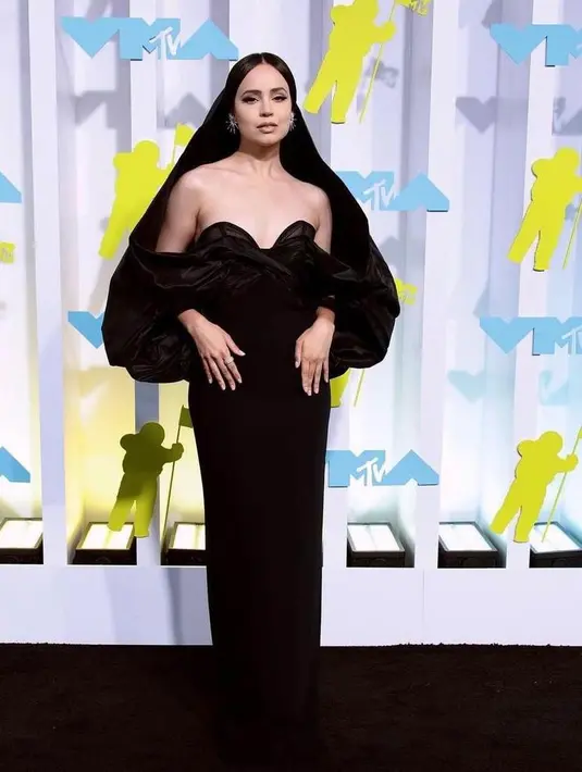 Sofia Carson tampil stunning mengenakan gaun hitam dengan detail sweetheart neckline dan oversized hoot rancangan Carolina Herrera. (Instagram/lofficielthailand).