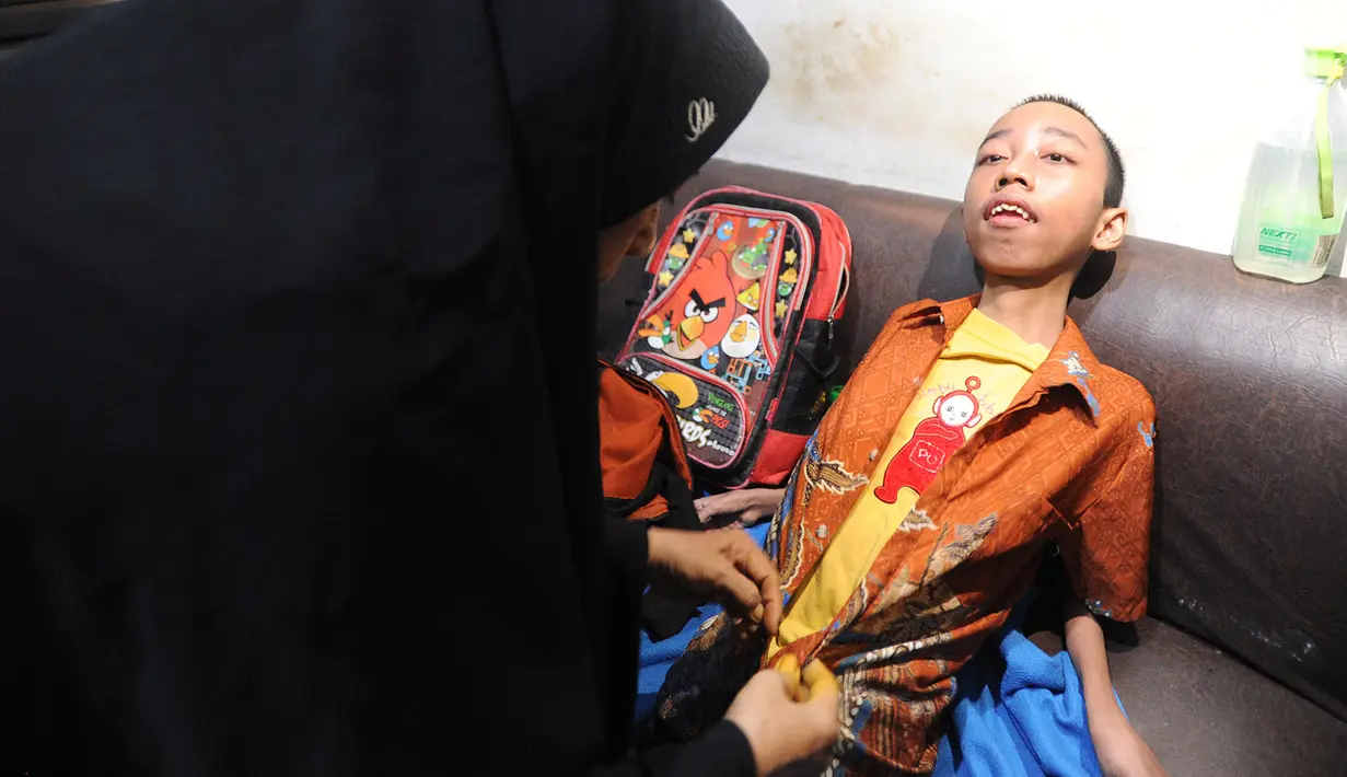 Setiap pagi, sang ibu memandikan dan memakaikan seragam SMP, pakaian kebanggaan Fauzan Akmal Maulana. Lalu, setelah disuapi sarapan oleh sang ibu, Fauzan digendong sang ibu menuju sekolah. (merdeka.com/Arie Basuki)