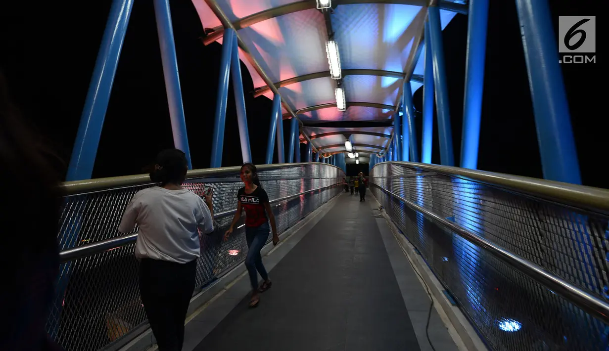 Warga melintasi jembatan penyeberangan orang (JPO) berhias lampu warna-warni di kawasan Jakarta Timur, Kamis (27/12).JPO ini memiliki struktur dan bentuk yang artistik dengan dihiasi lampu yang bisa berganti-ganti warna. (Merdeka.com/Imam Buhori)