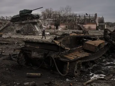 Seorang perempuan berjalan melewati tank yang hancur di kota Trostyanets, Ukraina, Senin, 28 Maret 2022. Trostsyanets baru-baru ini direbut kembali oleh pasukan Ukraina setelah dikuasai oleh Rusia sejak awal perang. (AP Photo/Felipe Dana)