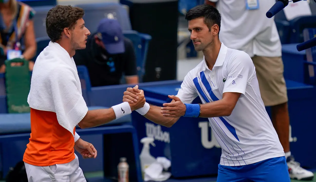 Petenis Serbia, Novak Djokovic berjabat tangan dengan Pablo Carreno Busta dari Spanyol usai gagal pada putaran keempat US Open 2020, di Flushing Meadows, (6/9/2020). Djokovic didiskualifikasi dari AS Terbuka 2020 setelah secara tidak sengaja memukul hakim garis dengan bola. (AP Photo/Seth Wenig)