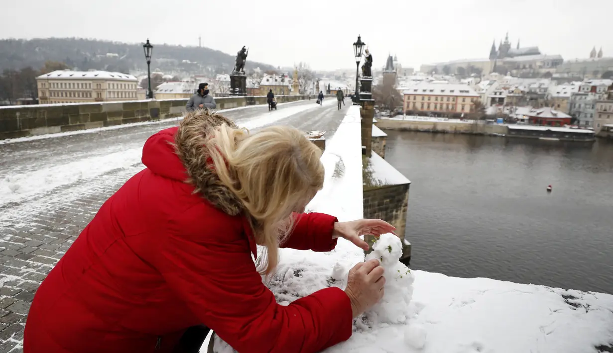 Seorang wanita membangun manusia salju di Jembatan Charles abad pertengahan setelah hujan salju pertama di Praha, Republik Ceko (3/12/2020). (AP Photo / Petr David Josek)