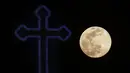 Supermoon terlihat di belakang salib dari gereja Ortodoks Kristen di pinggiran Lakatamia, Nicosia, Siprus, Selasa (7/4/2020). Fenomena dimana bulan berada pada titik terdekat dengan bumi ini merupakan penampakan supermoon terbesar di tahun 2020. (AP Photo/Petros Karadjias)