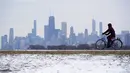 Seorang pria mengendarai sepedanya di dekat debu tipis salju di Pantai Montrose di Chicago (17/1/2022). Badai salju Chicago diperkirakan akan membawa hingga 5 inci di sepanjang Danau Michigan. (AP Photo/Nam Y. Huh)
