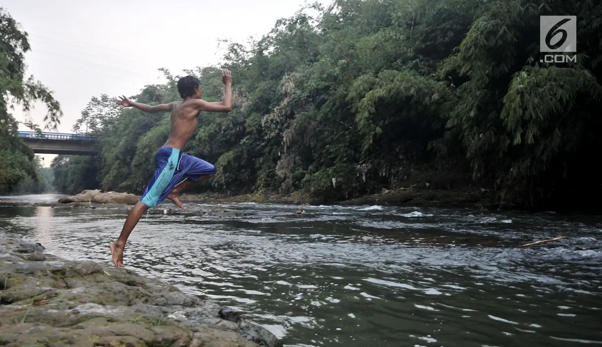 Seorang anak melompat ke Sungai Ciliwung, Depok, Jawa Barat, Kamis (4/7/2019). Menurunnya debit air Sungai Ciliwung akibat musim kemarau dimanfaatkan warga setempat sebagai tempat wisata gratis untuk mengajak anak berenang. (merdeka.com/Iqbal Nugroho)