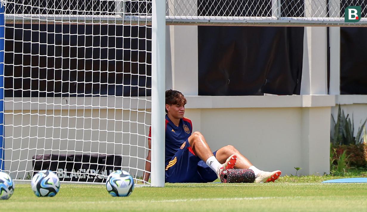 Pemain Timnas Spanyol U-17, Marc Guiu (kiri), mencari tempat teduh saat menjalani latihan dibawah sinar terik matahari yang berlangsung di Lapangan Sriwaru, Kecamatan Laweyan, Kota Solo, Rabu (8/11/2023). (Bola.com/Radifa Arsa)