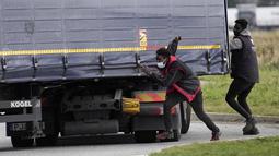 Para migran mencoba melompati truk untuk menyeberangi terowongan menuju Inggris di Calais, Prancis pada 14 Oktober 2021. Dalam praktik berbahaya dan berpotensi mematikan, ia mencoba melewati terowongan yang dijaga ketat yang menghubungkan kedua negara dengan bersembunyi di truk (AP/Christophe Ena)