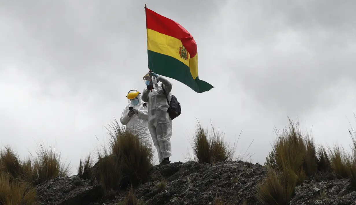 Petugas kesehatan APD lengkap mengibarkan bendera Bolivia saat dua kondor Andes dilepaskan ke alam liar di pinggiran Choquekhota, Bolivia, Selasa (23/2/2021). Dua burung kondor Bolivia yang terancam punah dilepaskan setelah pulih akibat terjatuh pada Februari. (AP Photo/Juan Karita)