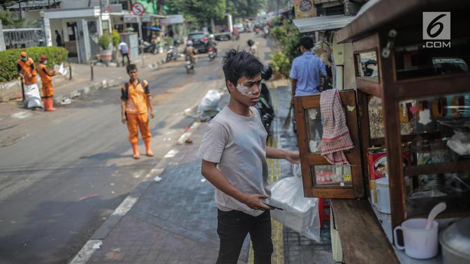 Pedagang menggunakan odol diwajah menghindari sisa gas air mata pasca bentrok massa dengan aparat di Palmerah, Jakarta, Kamis (26/9/2019). Banyak masyarakat yang melintas dan warga sekitar perih pada mata hingga bersin akibat sisa gas air mata pasca bentrokan kemarin. (Liputan6.com/Faizal Fanani)