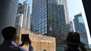 Warga menyaksikan Alain Robert yang dijuluki 'French Spiderman' memanjat gedung pencakar langit Cheung Kong Center di Hong Kong, Jumat (16/8/2019). Pria berusia 57 tahun tersebut memanjat Cheung Kong Center dalam kondisi panas dan lembab pada Jumat pagi. (Lillian SUWANRUMPHA/AFP)