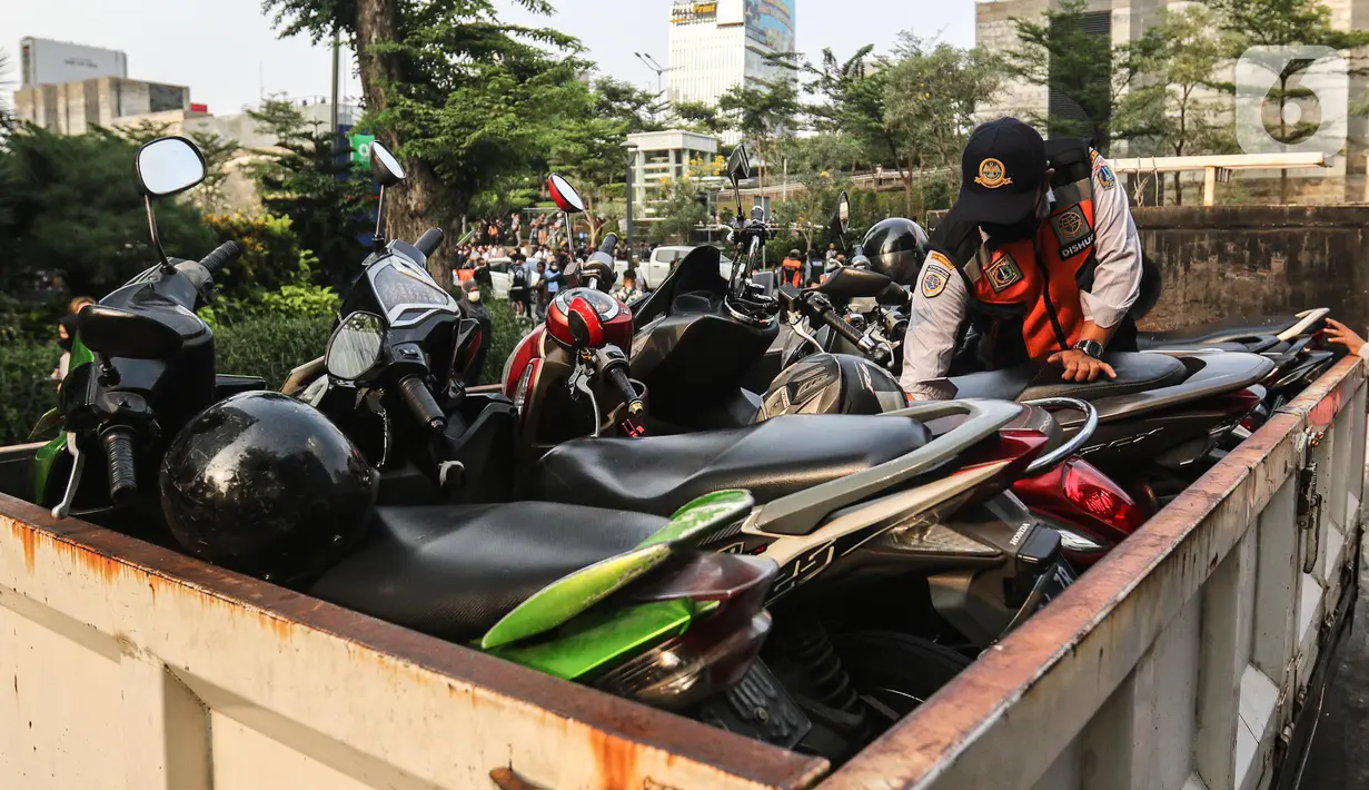 Petugas gabungan yang terdiri dari Satpol PP dan Dinas Perhubungan (Dishub) DKI Jakarta menata motor yang terjaring razia parkir liar di lokasi Citayam Fashion Week, kawasan Stasiun Dukuh Atas, Sudirman, Selasa (26/7/2022). Dishub DKI Jakarta mengamankan sebanyak 16 sepeda motor yang terpakir secara liar. (Liputan6.com/Faizal Fanani)