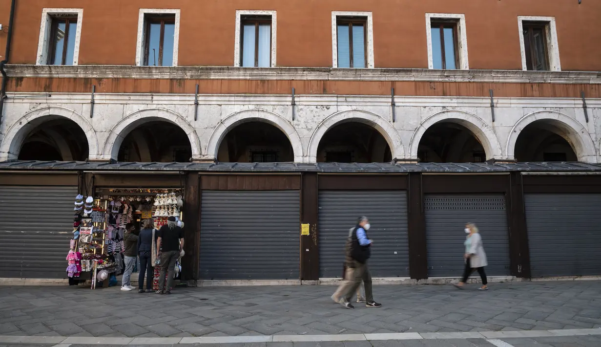 Orang-orang berjalan melewati toko-toko yang tutup di dekat Jembatan Rialto di Venesia pada 20 Mei 2021. Turis kembali berdatangan menikmati keindahan Venesia, yang sering dijuluki kota paling romantis di dunia, setelah Italia menghapus kewajiban karantina bagi pendatang. (Marco Bertorello/AFP)