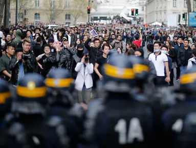 Polisi anti huru hara berjaga didepan para demonstran di Place de la Republique, di Paris, Prancis (2/4). Setidaknya 6.000 orang yang tergabung dalam komunitas etnis China di Prancis turun ke jalanan kota Paris menggelar aksi protes. (AFP/Benjamin Cremel)