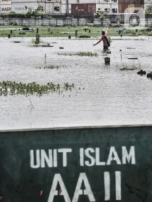 Amir (38) saat menjala ikan di genangan air yang merendam kompleks pemakaman TPU Semper, Jakarta, Selasa (2/2/2021). Banjir tersebut dimanfaatkan warga setempat untuk mencari ikan dengan menggunakan alat pancing serta jala. (merdeka.com/Iqbal S. Nugroho)