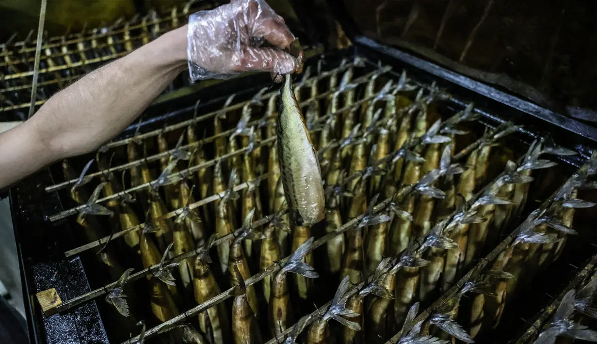Seorang pemuda Palestina mengasapi makarel untuk dijual di pasar ikan menjelang liburan Idul Fitri di kota Rafah di Jalur Gaza selatan (3/5/2021). Ikan makarel yang diolah melalui metode pengasapan ini merupakan hasil tangkapan nelayan Palestina melaut. (AFP/Said Khatib)