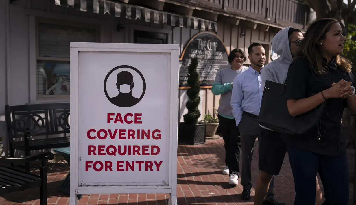 Orang-orang melewati tanda yang meminta pelanggan memakai masker di Laguna Beach, California, Senin (17/5/2021). California tidak akan mencabut aturan masker hingga 15 Juni untuk memberikan waktu persiapan kepada publik dan bisnis serta memastikan kasus COVID-19 tetap rendah. (AP Photo/Jae C. Hong)
