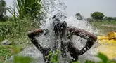 Seorang pria mandi di bawah air yang mengalir dari pipa di sepanjang dataran Yamuna pada suatu sore di New Delhi pada tanggal 29 Mei 2024. (Arun SANKAR/AFP)