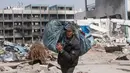 Seorang warga Palestina membawa barang-barangnya setelah mengunjungi rumah mereka yang hancur akibat serangan Israel di Khan Younis, Jalur Gaza, Rabu, 6 Maret 2024. (AP Photo/Mohammed Dahman)