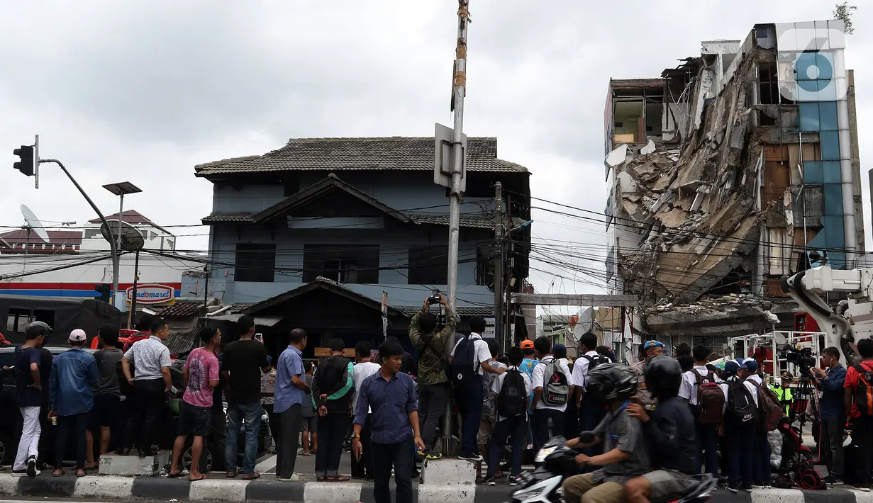 Warga menyaksikan gedung yang ambruk di Jalan Brigjen Katamso, Kota Bambu Selatan, Palmerah, Jakarta Barat, Senin (6/1/2020). Tiga orang dilaporkan terluka akibat tertima material gedung empat lantai tersebut. (Liputan6.com/Johan Tallo)