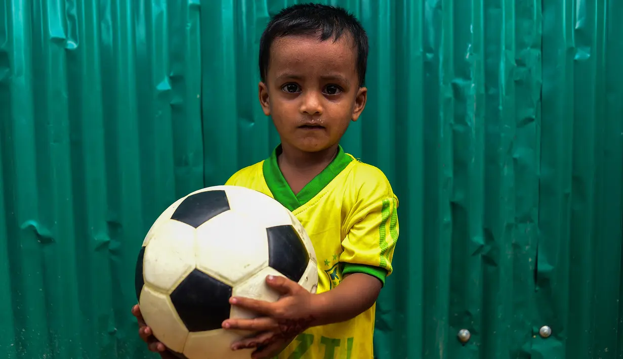 Seorang anak Rohingya mengenakan jersey timnas Brasil sambil memegang bola di kamp pengungsi Kutupalong di Ukhia, Bangladesh, 19 Juli 2018. Bagi pengungsi anak-anak Rohingya, Piala Dunia 2018 ini adalah ajang pertama bagi mereka. (AFP/Munir UZ ZAMAN)