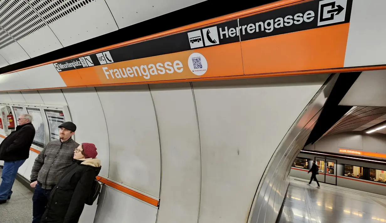 Para pelancong menunggu kereta bawah tanah U3 mereka di stasiun Herrengasse (Jalan Pria) yang ditutup dengan tanda sementara Frauengasse (Jalan Wanita) untuk merayakan Hari Perempuan Internasional di Wina, Austria, Rabu (8/3/2023). Dalam bahasa Inggris, ini berarti mengubah nama dari "Men's Lane" menjadi "Women's Lane". (JOE KLAMAR / AFP)