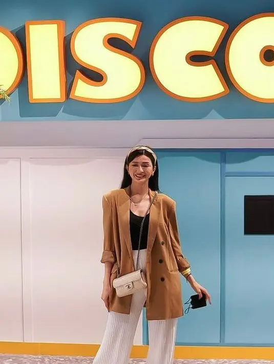 Adapula Furry Citra terlihat mengenakan blazer oversize warna cokelat dengan inner tanktop hitam, dipadukan celana plisket putih. Slingbag putih dan bandana pun melengkapi penampilannya. @senayancity