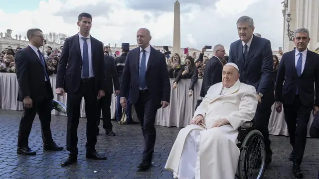 Paus Fransiskus dibantu oleh ajudannya saat audiensi publik di St. Peter's Square di Vatikan, Rabu 6 Maret 2024, ia tak bisa naik mobil kepausan sehingga memilih kursi roda. (AP/Gregorio Borgia)