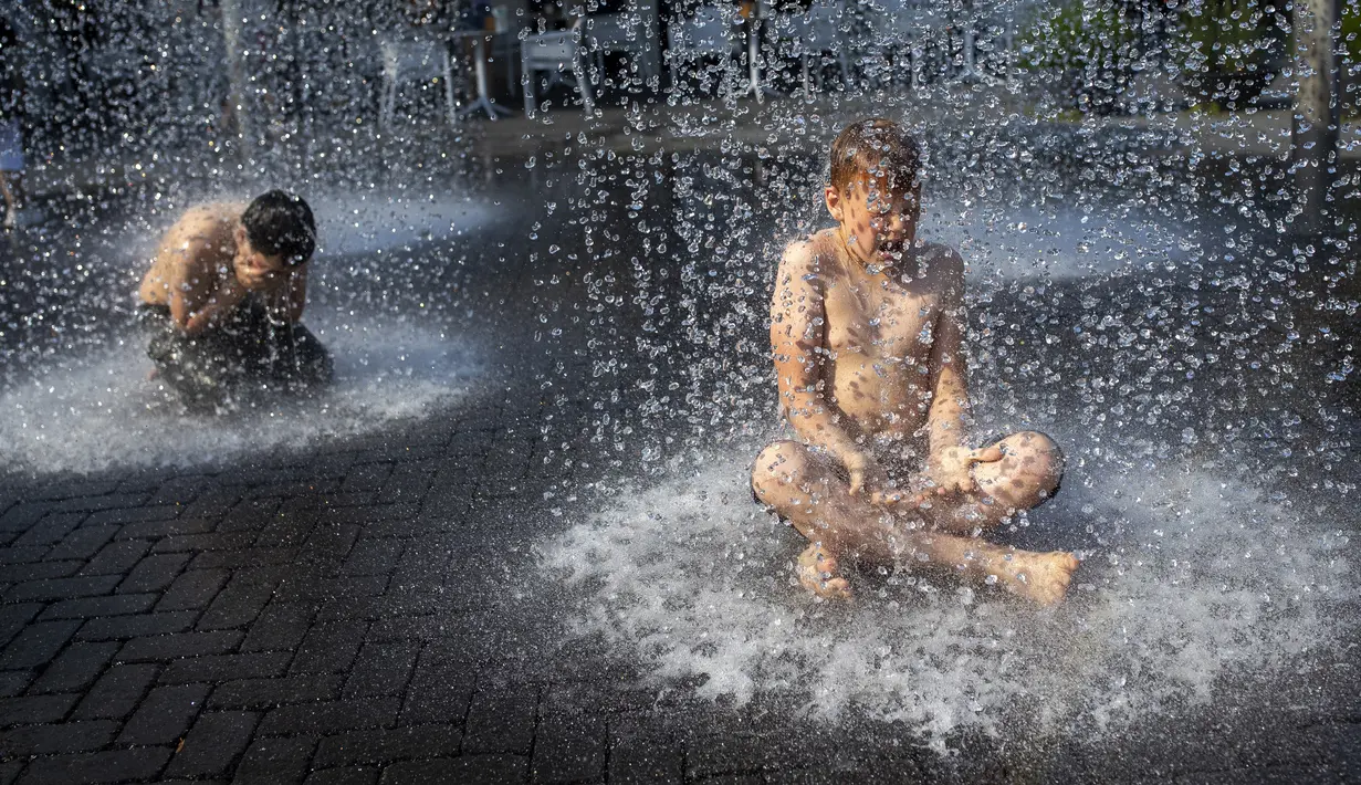 Anak-anak mendinginkan diri di air mancur umum di Vilnius, Lithuania, 26 Juni 2022. Gelombang panas berlanjut di Lithuania saat suhu naik hingga 32 derajat Celcius (89,6 derajat Fahrenheit). (AP Photo/Mindaugas Kulbis)