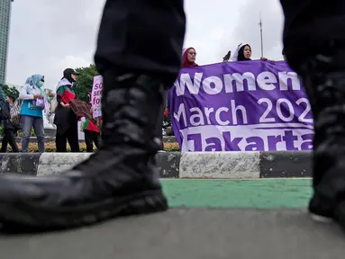 Seorang petugas polisi berjaga-jaga saat para aktivis membentangkan spanduk dalam unjuk rasa Hari Perempuan Internasional di Jakarta, Indonesia, Jumat, 8 Maret 2024. (AP Photo/Dita Alangkara)