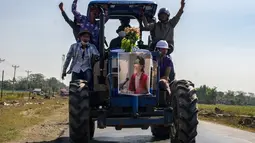 Para petani mengendarai traktor membawa poster pemimpin sipil Myanmar Aung San Suu Kyi yang ditahan saat demonstrasi menentang kudeta militer di Thongwa, di Yangon (12/2/2021). Demonstran yang berlangsung di Myanmar sendiri membuat hampir seluruh pekerja di berbagai perusahaan mogok kerja. (AFP/STR)