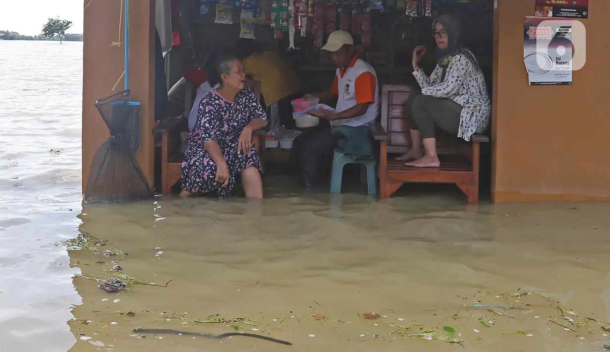 Warga berada di salah satu warung yang terendam banjir di Desa Sukalaksana Kabupaten Bekasi, Jawa Barat, Senin (22/02/2021). Jebolnya tanggul Sungai Citarum ini disebabkan oleh debit air yang tinggi. (Liputan6.com/Herman Zakharia)