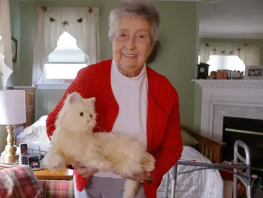 Mary Derr (93) menggendong robot kucing yang dipanggil "Buddy" di rumahnya, South Kingstown di Rhode Island, 1 Desember 2017. Buddy adalah robot berbentuk hewan peliharaan bernama 'Joy for All' untuk pendamping lanjut usia (lansia). (AP/Stephan Savoia)