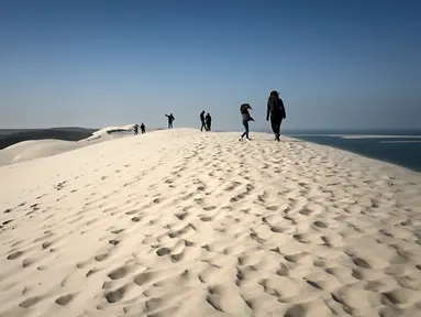 Orang-orang menikmati hari yang cerah di "Dune du Pilat" di La Teste-de-Buch, dekat Teluk Arcachon di barat daya Prancis pada 3 April 2021. The Dune of Pilat merupakan gurun pasir tertinggi di Eropa, yaitu sekitar 110 meter di atas permukaan air laut. (Philippe LOPEZ / AFP)