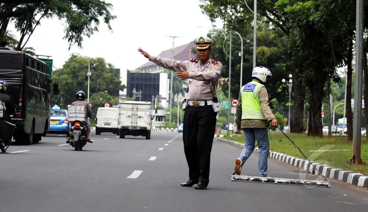 Petugas Polisi menertibkan jalan saat relawan Saber membersihkan ranjau paku di depan Istana Merdeka, Jakarta, Jumat (6/3/2015). Paku yang ditebar oleh orang tidak bertangung jawab seringkali mengganggu para pengguna jalan. (Liputan6.com/Faizal Fanani)