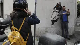 Seorang pria berselfie di dekat mural pelatih Jose Mourinho mengendarai skuter Vespa berhias lambang AS Roma di lingkungan Testaccio,  Roma (7/5/2021). Jose Mourinho dipecat Tottenham Hotspur pada 19 April kemarin. (AP Photo/Gregorio Borgia)
