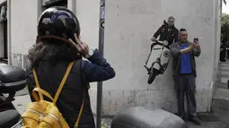 Seorang pria berselfie di dekat mural pelatih Jose Mourinho mengendarai skuter Vespa berhias lambang AS Roma di lingkungan Testaccio,  Roma (7/5/2021). Jose Mourinho dipecat Tottenham Hotspur pada 19 April kemarin. (AP Photo/Gregorio Borgia)