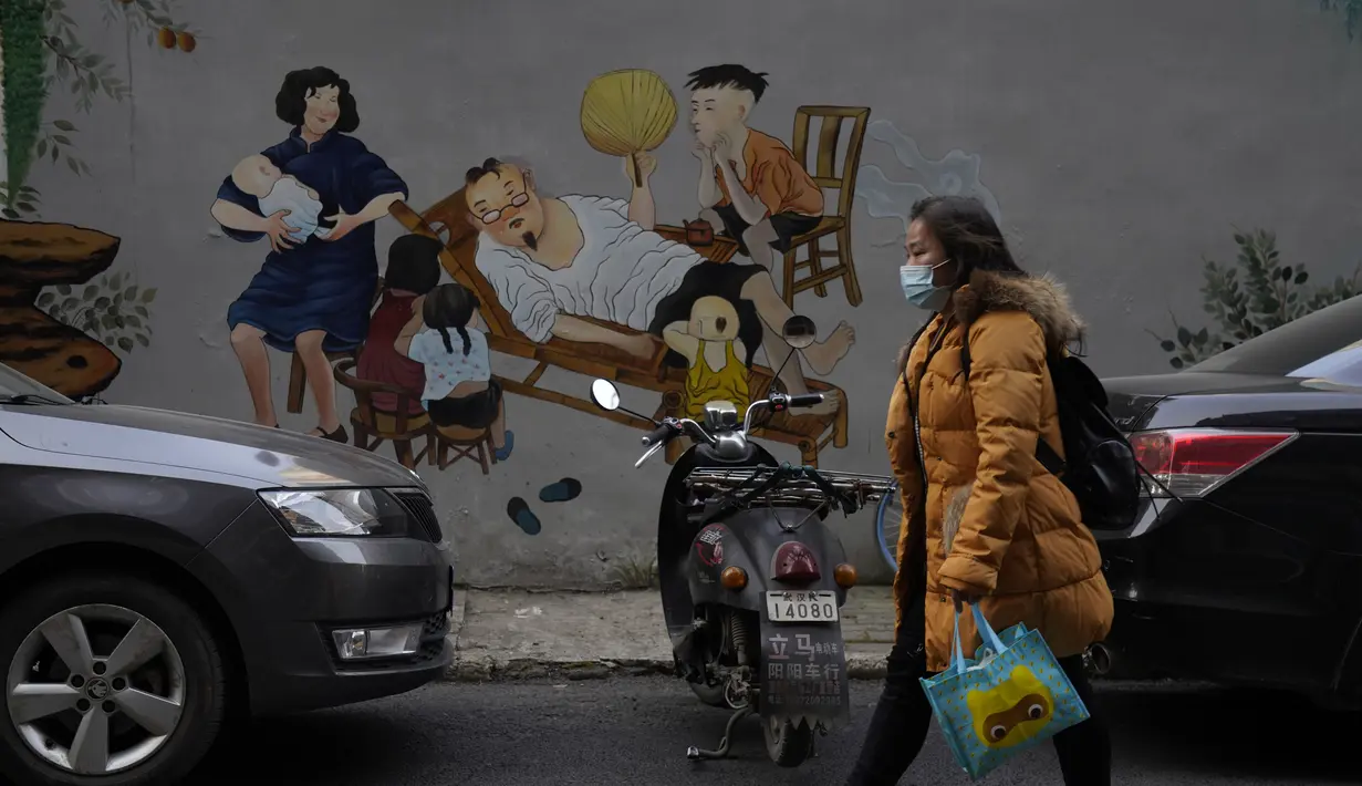 Seorang warga bermasker melewati mural yang menggambarkan kehidupan rumah tangga yang indah di Wuhan di provinsi Hubei, China, Jumat (15/1/2021). Selain masker, orang-orang menjalani kehidupan sehari-hari mereka seperti sebelumnya di kota pertama kali virus corona terdeteksi. (AP Photo/Ng Han Guan)