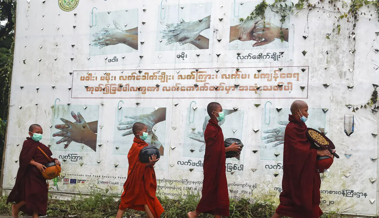 Biksu Buddha mengenakan masker berjalan melewati papan peringatan COVID-19 saat mereka mengumpulkan sedekah pagi di Yangon, Myanmar, Kamis (15/7/2021). Hampir 90 persen wilayah di Myanmar telah terkena dampak gelombang ketiga Covid-19. (AP Photo/Thein Zaw)