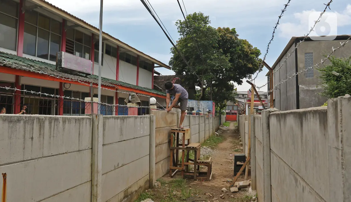 Warga memanjat tembok untuk memasuki rumahnya di kawasan Ciledug, Kota Tangerang, Banten, Senin (15/3/2021). Tembok beton sepanjang 300 meter dengan tinggi 2 meter serta dipasang kawat duri itu menutup akses menuju rumah dan tempat usaha milik warga. (Liputan6.com/Herman Zakharia)
